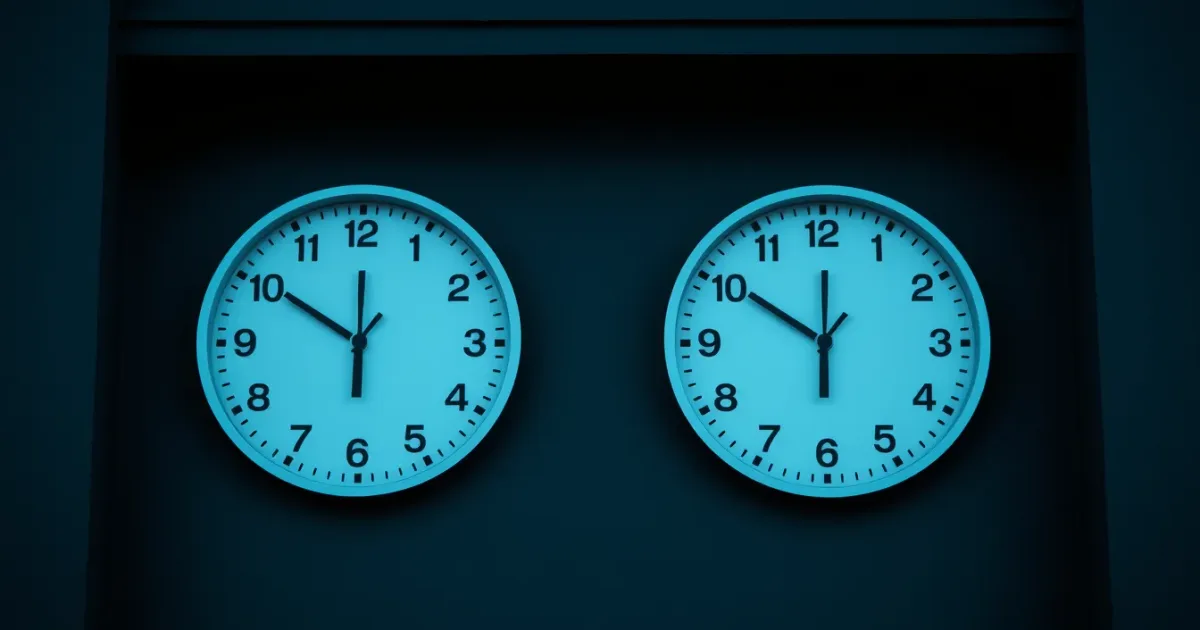 Two clocks on a dark wall showing different hours, illustrating statutory maternity pay and US tax