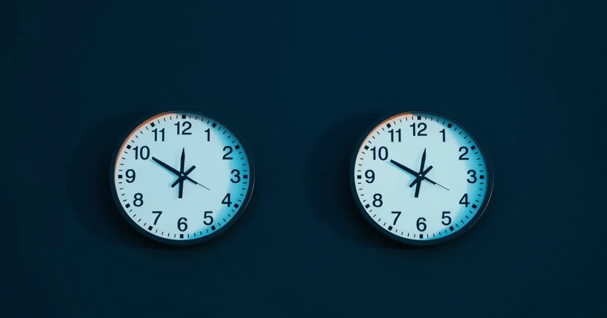 Two clocks on a dark wall showing different hours, illustrating article 20A and US academics in Britain