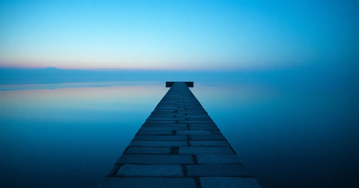 A stone causeway running out across still water at dusk, illustrating W-8BEN-E for a UK company